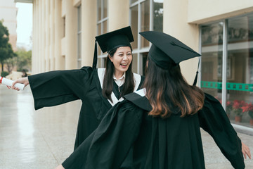 Happy graduated young multi ethnic students hugging. beautiful smart university learner finished college sending care love emotion to friend classmate smiling laughing open arms hands out building