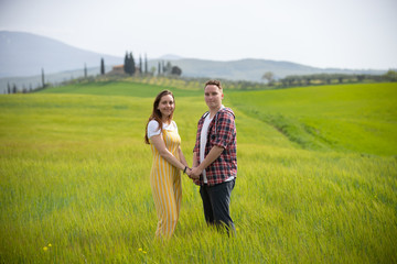 Naklejka na ściany i meble A young happy couple standing on a green meadow holding hands
