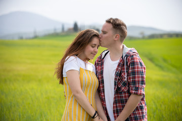 A young happy couple standing on a green meadow. A man kiss his girlfriend in a forehead