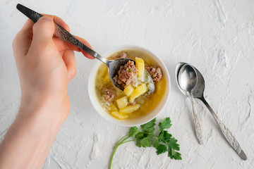 first person view of a person eat steaming soup with meatballs using a metal tableware on a white tables