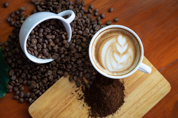 White coffee mugs and coffee beans Poured on a wooden table, beautifully arranged, decorated with coffee leaves. Is a mixture of raw materials for making coffee