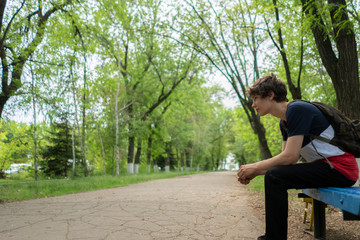 a male sitting on the bench in the city park alley during summers