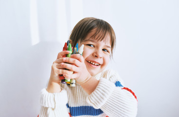 Closeup portrait of cute little girl smiling and playing with colorful pencils, looking to the camera. Beautiful kid holding colorful pencils in her hands, posing at home. People, childhood, education