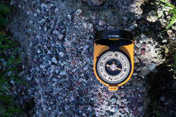 Naklejka premium Orange compass with a mirror on the rocks shows the way to the tourist, space for text