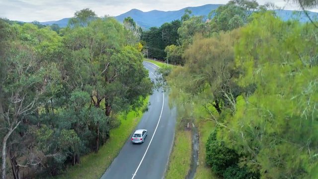 Slow aerial rise over cars driving on rural road revealing scenic countryside and mountains in Healesville, Victoria, Australia