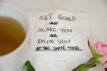 Planning motivational quote on white napkin on white table with tea, rose and pen. Set goals that scare you and excite you at the same time