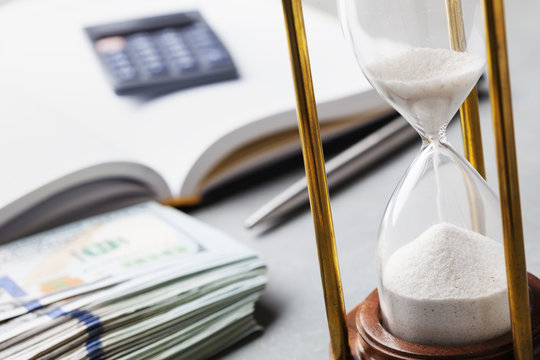 Dollar bills, hourglass and notebook for planning investments or cash expenses.