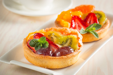 Photo of a fruit and berry tart dessert with toss sugar on wooden background. Fresh delicious sweet cake with raspberries, grapes, strawberries, cherry, kiwi, grapefruit and cream.
