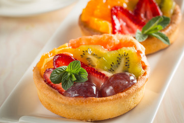 Photo of a fruit and berry tart dessert with toss sugar on wooden background. Fresh delicious sweet cake with raspberries, grapes, strawberries, cherry, kiwi, grapefruit and cream.