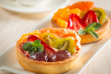 Photo of a fruit and berry tart dessert with toss sugar on wooden background. Fresh delicious sweet cake with raspberries, grapes, strawberries, cherry, kiwi, grapefruit and cream.