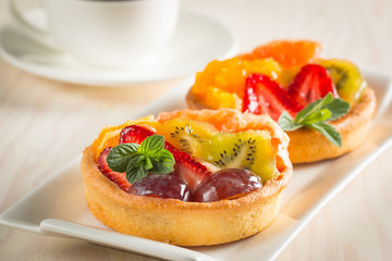 Photo of a fruit and berry tart dessert with toss sugar on wooden background. Fresh delicious sweet cake with raspberries, grapes, strawberries, cherry, kiwi, grapefruit and cream.