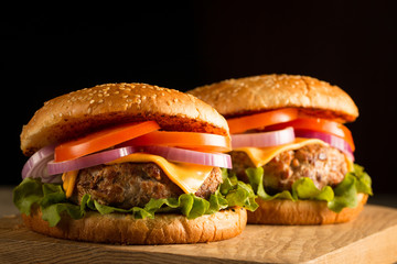 Home made hamburger with beef, onion, tomato, lettuce and cheese. Fresh burger close up on wooden rustic table with potato fries, beer and chips. Cheeseburger.