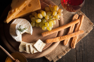 Cheese plate with brie, camambert, gauda with grapes,honey, crackers and nuts on a wooden background