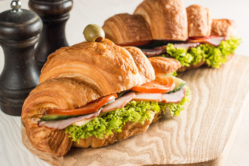 Photo of tasty and fresh croissant sandwich with salad, ham, cheese, tomatoes on wooden background. Morning breakfast concept. Healthy and fast food.