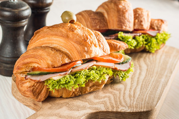 Photo of tasty and fresh croissant sandwich with salad, ham, cheese, tomatoes on wooden background. Morning breakfast concept. Healthy and fast food.