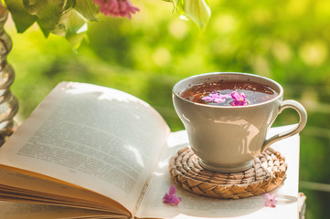 Book, glasses, cup of tea and lilac on a wooden window. Fragrant tea in the garden. Romantic...