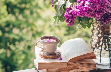 Book, glasses, cup of tea and lilac on a wooden window. Fragrant tea in the garden. Romantic...