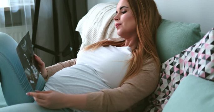 Pregnant woman on sofa looking her baby on ultrasound image