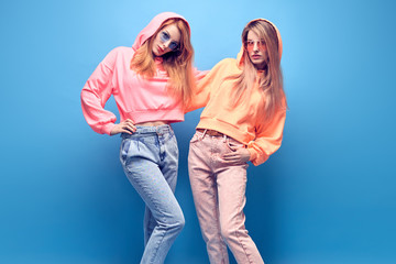 Fashion. Two hipster Girl in trendy colorful neon Outfit Fooling Around in Studio. Young Tomboy...