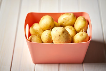 young potatoes in coral container on white  kitchen table