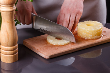 young woman in a gray apron cuts marinated pineapple