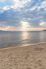 Fototapeta premium Promienie słoneczne lub promienie słoneczne wpadające przez chmury o wschodzie słońca na pięknej plaży