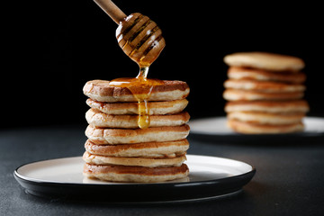 Stack of Pancakes with pouring honey on dark background. honey spoon