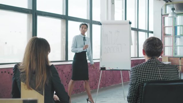 Young African American female manager holds a presentation near a flipchart and draws graphics. Coworking in loft style