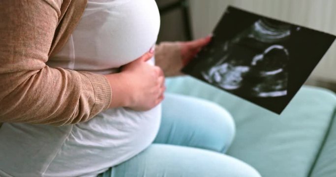 Pregnant woman on sofa looking her baby on ultrasound image