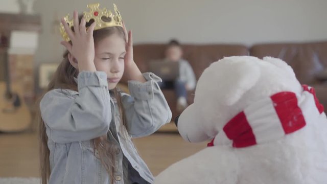 Portrait beautiful girl sit on the floor with huge taddy bear, girl have crown at her head which she put on white bear and hug this big toy