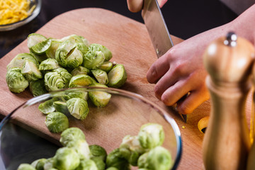 young woman cuts Brussels sprouts on a wooden cutting board