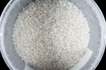 Pure white rice in a plastic bucket on a black background, isolate.