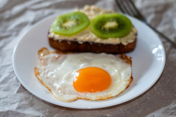 Delicious and healthy breakfast. Fried eggs and kiwi sandwich on a white plate, close-up, space for text