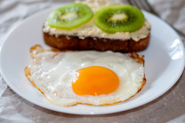 Delicious and healthy breakfast. Fried eggs and kiwi sandwich on a white plate, close-up, space for text