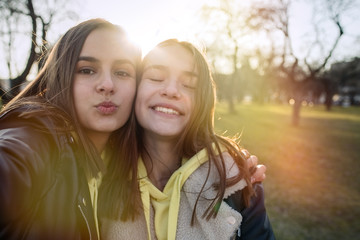 Obraz premium Two happy teenage friends taking selfie with mobile phone while walking in the park