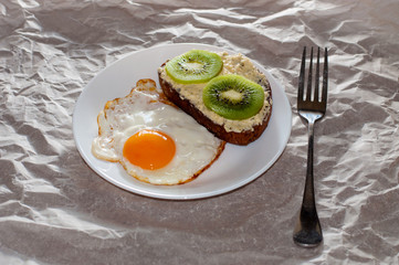 Delicious and healthy breakfast. Fried eggs and kiwi sandwich on a white plate, close-up, space for text