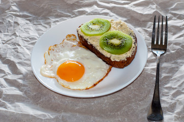 Delicious and healthy breakfast. Fried eggs and kiwi sandwich on a white plate, close-up, space for text