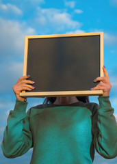 Girl holding chalkboard at face level, against the sky with clouds. Copy space for your text design. billboard, chalk, advertising poster.