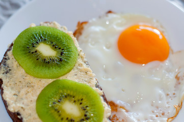 Healthy and tasty breakfast, wholemeal bread sandwich with kiwi and a fried egg on a white plate, close-up, top view