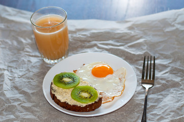 Healthy and tasty breakfast, juice, wholegrain sandwich with kiwi and fried egg on white plate
