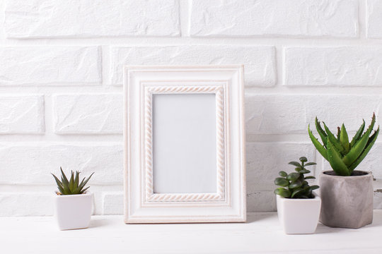 Empty frame mockup and succulents and cactus plants in pots  near by white brick wall.