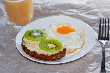 Healthy and tasty breakfast, juice, wholegrain sandwich with kiwi and fried egg on white plate