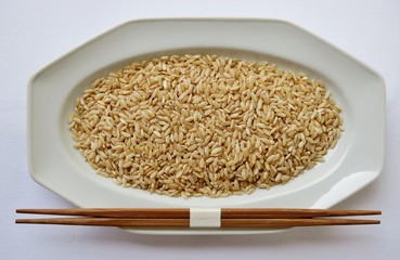 unpolished brown rice on a white plate with chopsticks
