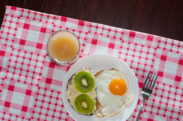 Healthy and tasty breakfast, quince juice, whole-grain bread sandwich with kiwi and egg on white plate, pink napkin