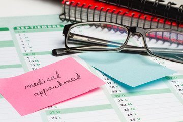 Post it medical appointment sobre calendario  junto a una agenda y unas gafas. Vista de frente y de...