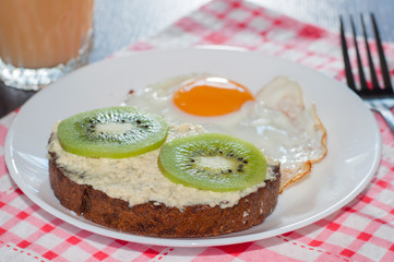 Healthy, tasty breakfast, juice, wholemeal bread sandwich with kiwi and a fried egg on white plate