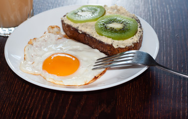 Healthy, tasty breakfast, juice, wholemeal bread sandwich with kiwi and a fried egg on a white plate, on a wooden table