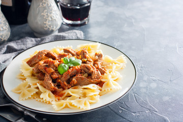 Beef in tomato sauce with farfalle on a white plate, horizontal, copy space