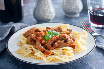 Beef in tomato sauce with farfalle on a white plate, horizontal
