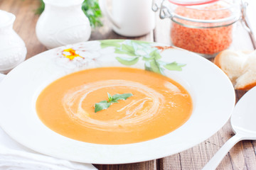 Red lentil cream soup in a white plate on a wooden table, horizontal